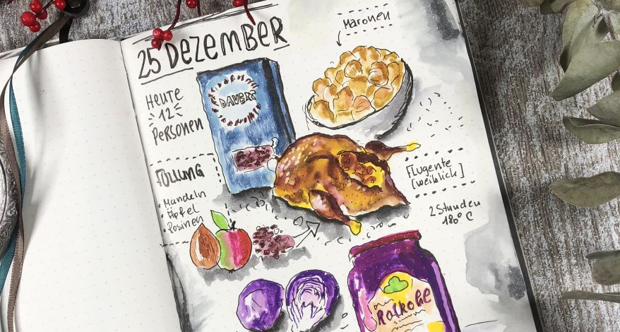 Ein aufgeschlageses Skizzenbuch zeigt als Aquarell gezeichnet die Zutaten eines Weihnachtsmenüs mit Gans, Rotkohl, Äpfeln, Maronen.