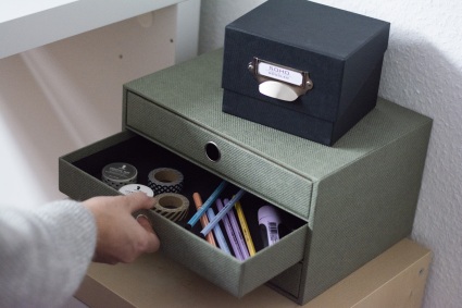 Hand öffnet Schublade der Schubladenbox aus der S.O.H.O.-Serie von Rössler. Sarin befinden sich Stifte und Washitape, auf der Schubladenbox steht eine kleine schwarze Box.