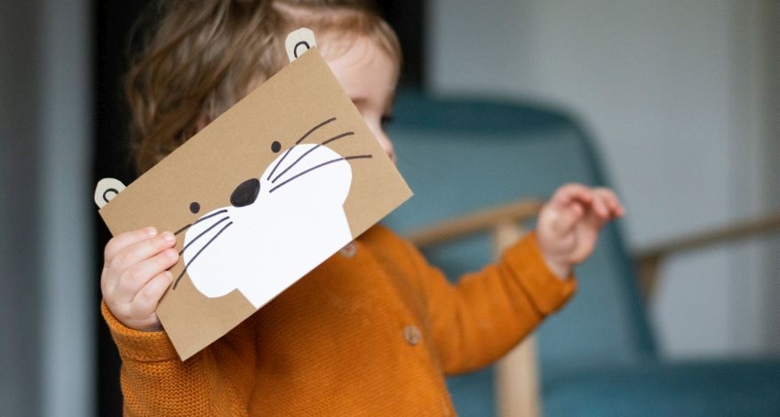 Ein Kleinkind hält eine Karte, gestaltet als Otter, in der Hand.