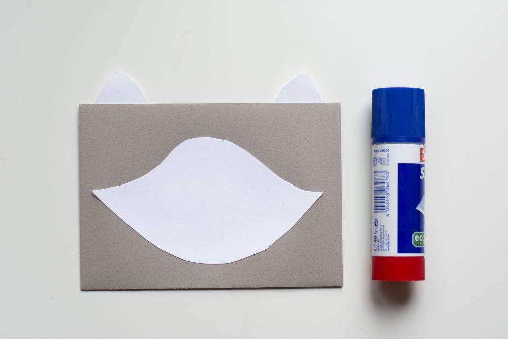 Bastelanleitung Einladungskarte zum Kindergeburtstag: Selbst gebastelte Do it yourself-Karte als Waschbär, Schritt 2: Papierzuschnitte sind auf Briefumschlag aufgeklebt