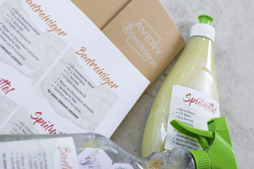 Rezepte von DIY-Haushaltsmitteln sind auf einen Etikettenbogen von Avery Zweckform gerdruckt. Daneben liegt eine Flasche mit DIY-Spülmittel.