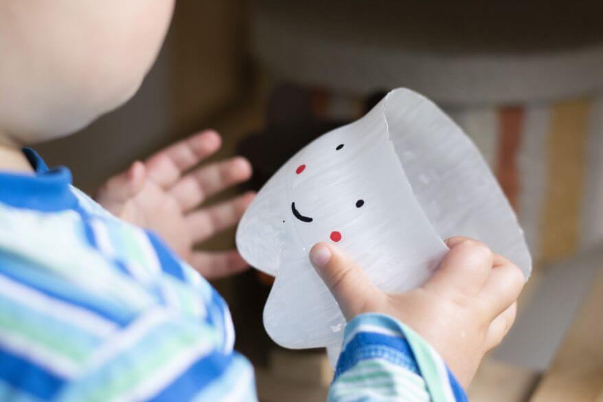 Ein Kind hält einen Zahnputzbecher aus einer PET-Flasche in der Hand. Dieser sieht aus wie ein Zahn.
