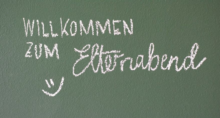 Eine Tafel wurde mit Kreide beschriftet. Auf ihr ist zu lesen "Willkommen zum Elternabend".