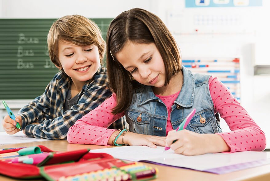 Ein Mädchen und ein Junge sitzen nebeneinander im Klassenzimmer am Tisch. Das Mädchen schreibt etwas mit einem Linkshänder Füller von Stabilo. Der Junge schaut ihr über die Schulter. Foto: Stabilo