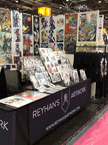 Ein schwarzer Messestand mit der Aufschrift Reyhans Artwork. Auf dem Tisch stehen Illustrationen im Hintergrund sind Plakate der Künstlerin aufgehängt. Foto: Reyhan Yildirim