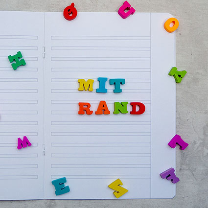 Auf einem Tisch liegt ein aufgeschlagenes Schreibheft der Marke Brunnen mit Lineatur für dritte Klasse und Rand. Auf dem Heft wurde mit bunten Radiergummi-Buchstaben "mit Rand" geschrieben, weitere Buchstaben sind auf dem Heft verteilt. Foto: Johanna Rundel