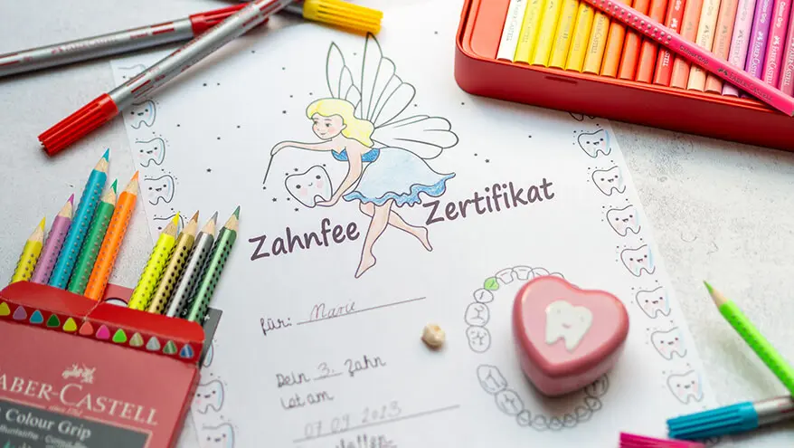 Ein ausgedrucktes Zahnfee-Zertifikat liegt auf einem grauen Untergrund. Rundherum sind verschiedenen Bunt- und Filzstifte der Marke Faber-Castell zu sehen. Foto: Johanna Rundel