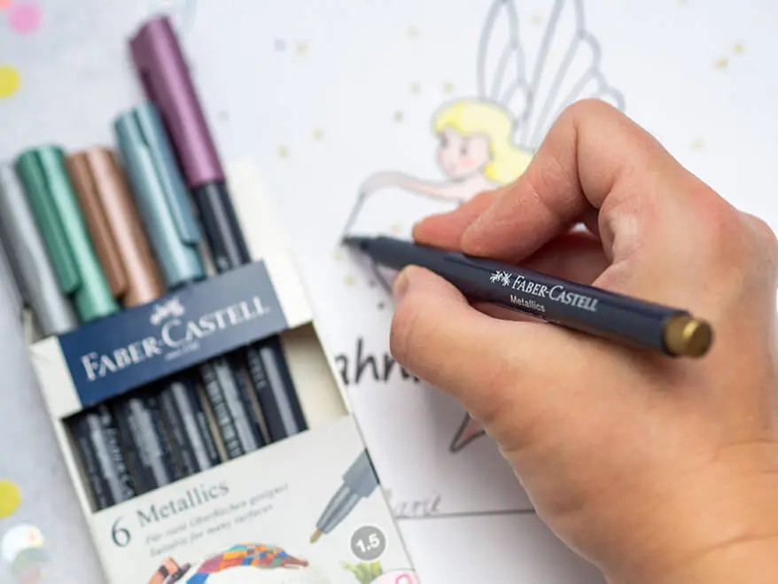 Jemand malt mit einem Metallic-Marker von Faber-Castell ein Zahnfee-Zertifikat aus. Eine Packung mit weiteren Markern liegt daneben. Foto: Johanna Rundel