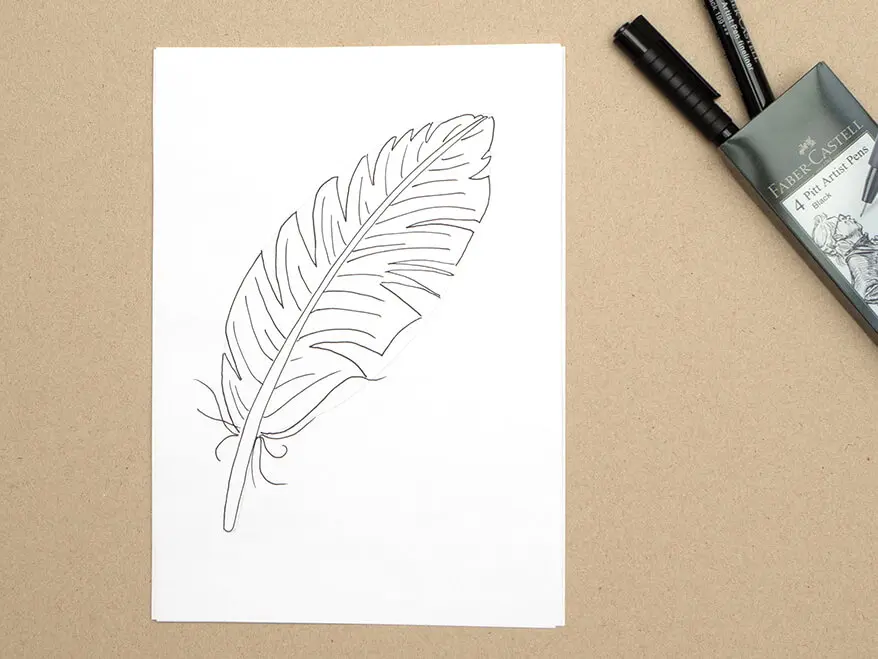 Auf ein Blatt wurde mit einem Pigmentliner von Faber-Castell der Umriss einer Vogelfeder gemalt. Ein Etui mit weiteren Finelinern liegt geöffnet daneben. Foto: Johanna Rundel