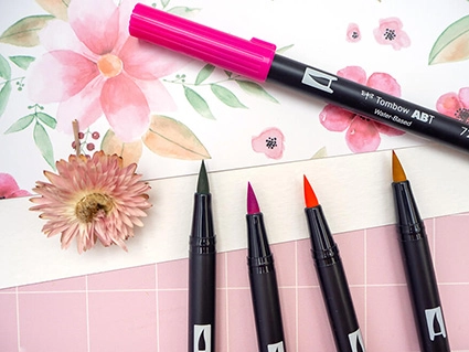 Geöffnete Brush Pens von Tombow liegen vor und auf einem Blatt Aquarellpapier, auf das Blumen gemalt wurden. Foto: Johanna Rundel