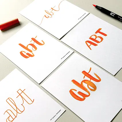 Auf mehrere Blätter wurde in unterschiedlichen Lettering-Stilen mit einem orangene Brush Pens das Wort "Abt" geschrieben.