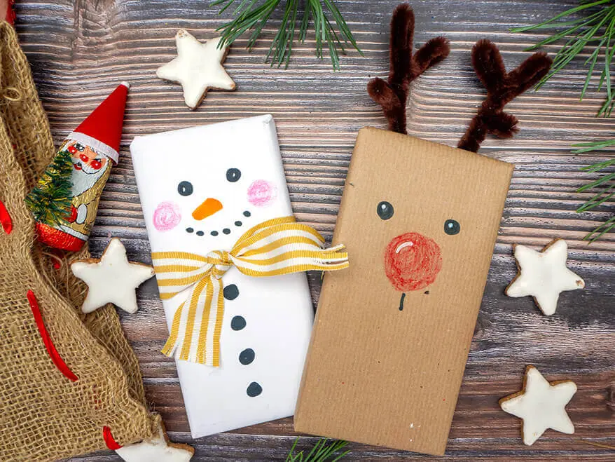 Auf einer rustikalen Holzplatte liegen zwei weihnachtlich verpackte und mit Stiften von STAEDTLER bemalte Schokoladentafeln. Foto: Johanna Rundel