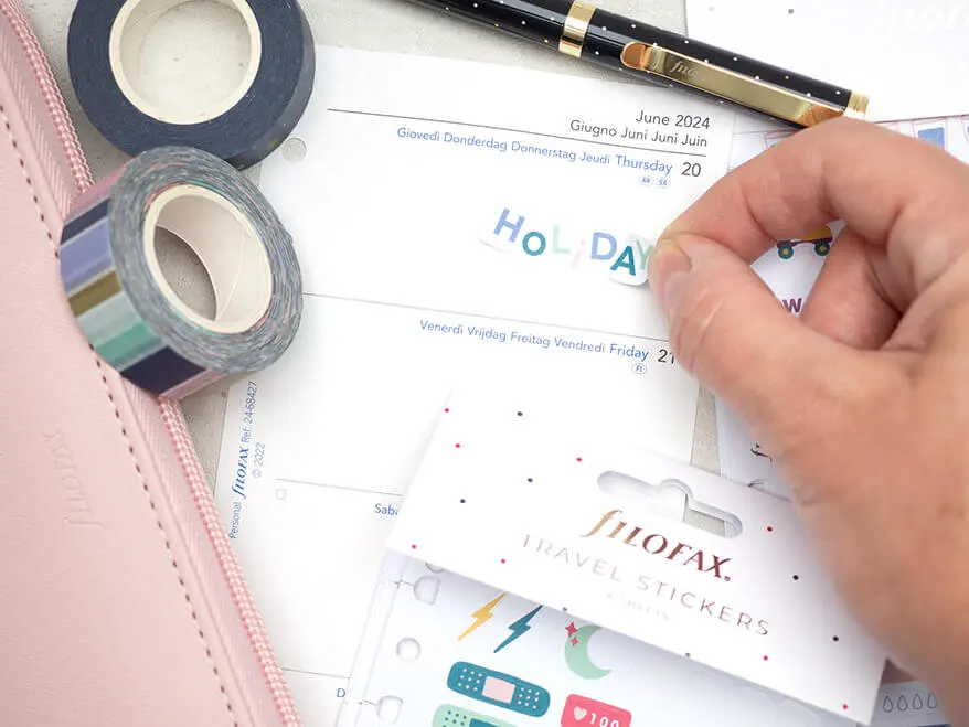 Jemand klebt einen Sticker in einen rosafarbenen Filofax-Organizer. Foto: Johanna Rundel