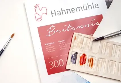 Ein Britannia 300 Aquarellblock von Hahnemühle umgeben von verschiedenen Künstlermaterialien.