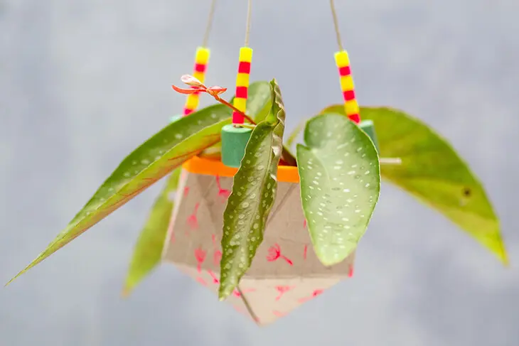 Vor einem hellen Hintergrund hängt ein selbstgebastelter Blumentopf aus einer Milchtüte, der mit Bastelmaterialien von HEYDA und KNORR prandell verschönert wurde.