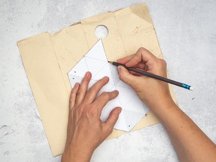 Jemand überträgt mit einem Bleistift eine Bastelvorlage auf einen Milchtütenkarton.
