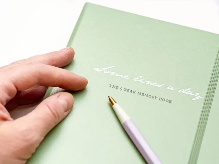 Eine Hand liegt auf einem hellgrünen Notizbuch von LEUCHTTURM1917 auf dem „Some Lines a Day“ steht. Foto: Johanna Rundel