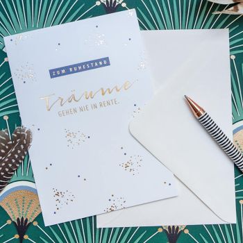 Eine Grußkarte von Grafik Werkstatt mit den Worten „Zum Ruhestand – Träume gehen nie in Rente“ liegt auf einem Untergrund im Art-Déco-Stil. Foto: Johanna Rundel