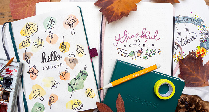 Auf einem rustikalen Holzbrett liegen drei Bullet Journal von LEUCHTTURM1917 mit aufgeschlagenen Monatsdeckblättern für Oktober 2024 in verschiedenen Stilrichtungen. Foto: Johanna Rundel