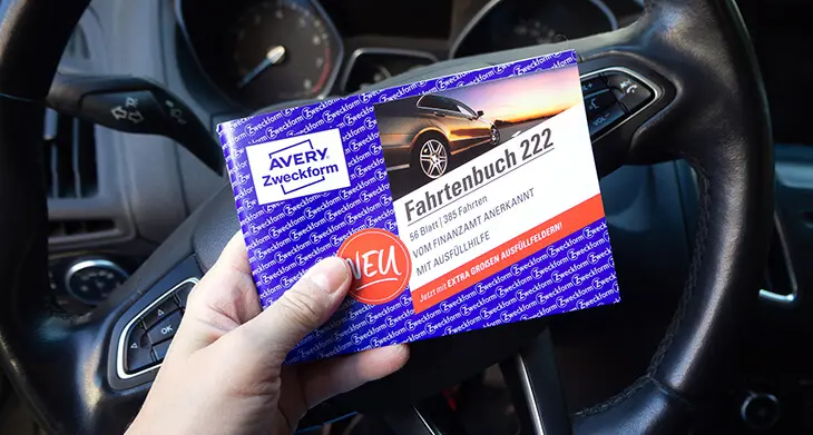 Jemand sitzt auf dem Fahrersitz eines Autos und hält ein Fahrtenbuch von Avery Zweckform in den Händen. Foto: Johanna Rundel
