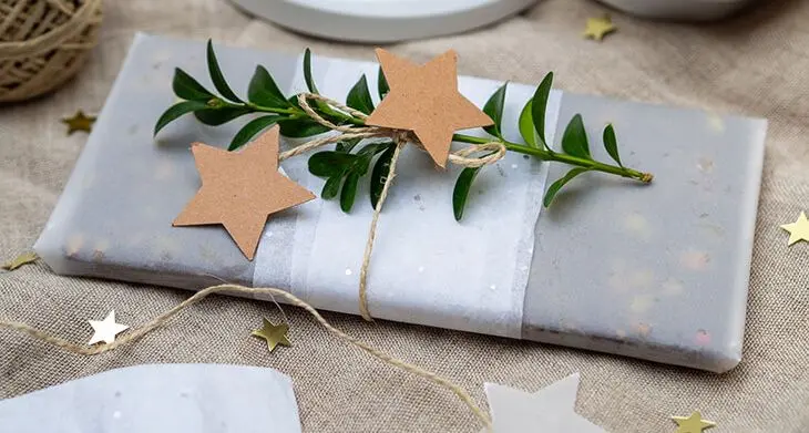 Eine Tafel selbstgemachte vegane Schokolade, hübsch verpackt in verschiedenen Papieren und Kordeln von HEYDA und KNORR prandell, liegt auf einem weihnachtlich dekorierten Tisch. Foto: Johanna Rundel