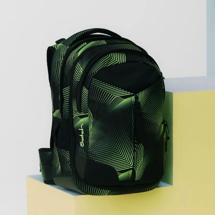 Ein grün-schwarz gemusterter Schulrucksack von satch steht auf einem hellen Podest vor einem hellen Hintergrund.