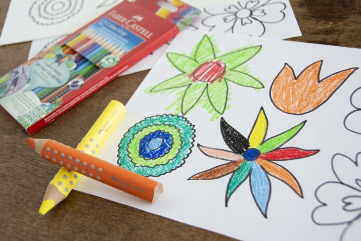 Eine bunt ausgemalte Malvorlage mit Blumen liegt zusammen mit Buntstiften von Faber-Castell auf einem Schreibtisch