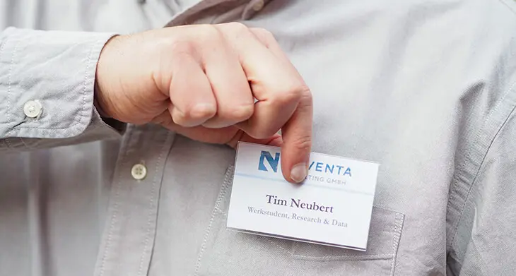 Jemand steckt sich ein Namensschild von Avery Zweckform an die Tasche seines hellgrauen Hemdes. Foto: Johanna Rundel