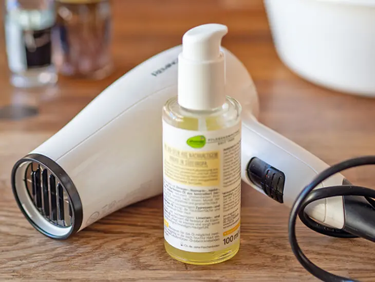 Hinter einer Kosmetikflasche mit Folienetikett liegt ein weißer Föhn. Foto: Johanna Rundel