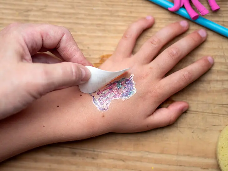 Jemand entfernt auf der Hand eines Kindes die Trägerfolie von einem Einhorn-Tattoo von Coppenrath. Foto: Johanna Rundel