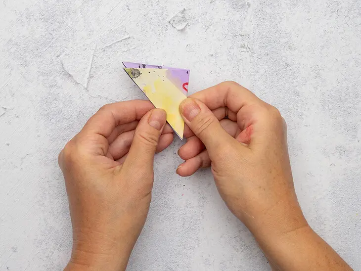 Jemand faltet ein bunt bemaltes Papierquadrat zu einem Dreieck. Foto: Johanna Rundel
