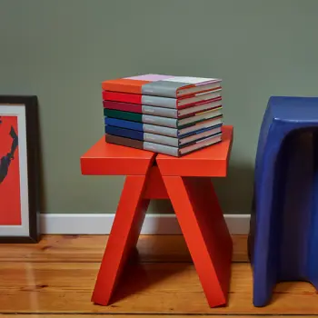 Mehrere Notizbücher von Semikolon liegen gestapelt auf einem roten Hocker.