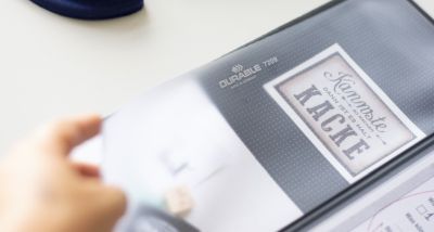 Eine Schreibtischunterlage der Marke Durable liegt auf einem weißen Untergrund. Eine Hand hält die Abdeckung der Unterlage nach oben.