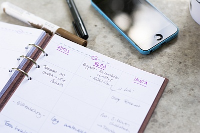 Offener Planer mit Content-Planung, Stifte und Smartphone auf einem Tisch.
