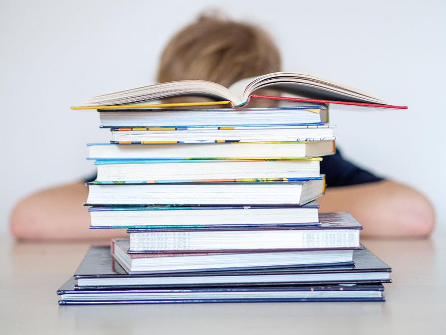 Ein Kind sitzt vor einem hohen Stapel Schulbücher. 
