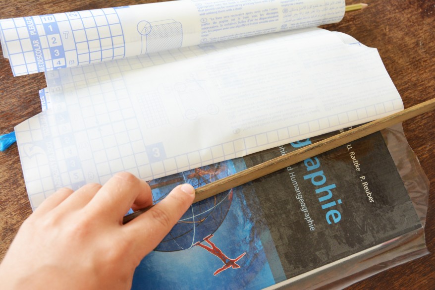 Ein Buch wird mithilfe eines Lineals mit Selbstklebefolie eingebunden.