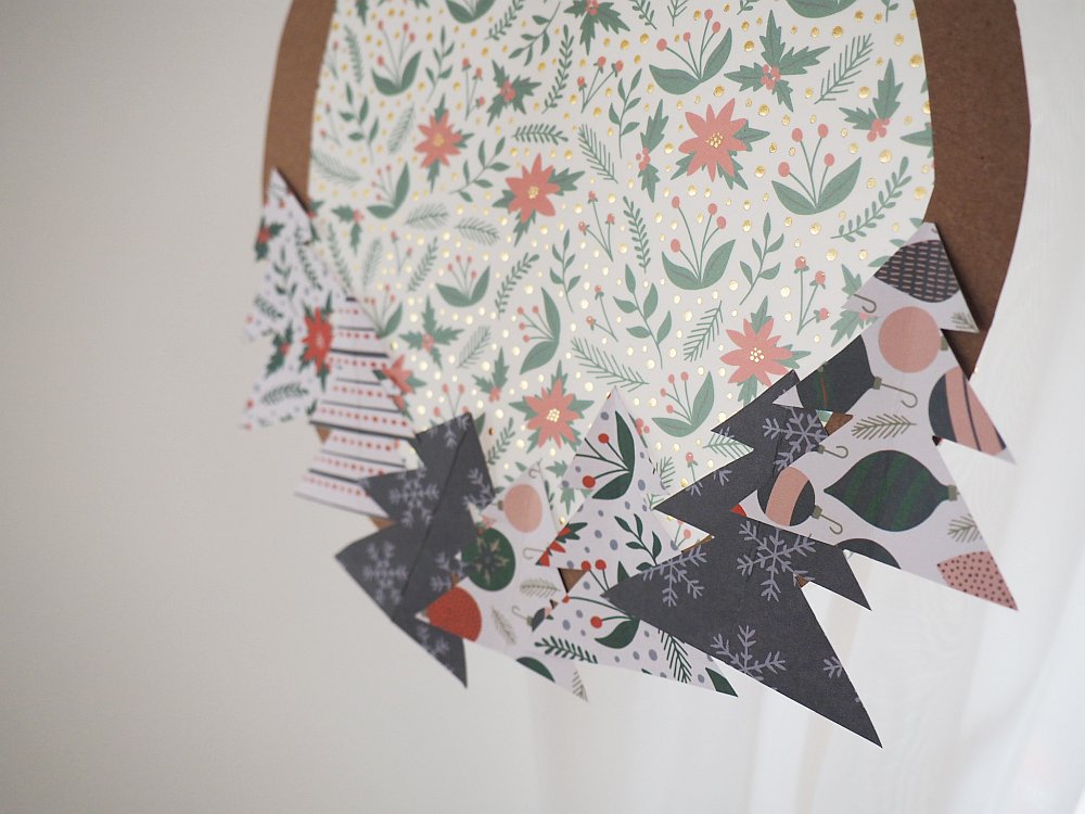 Nahaufnahme eines Papierkranzes mit Weihnachtsmotiven und Tannenbäumen.