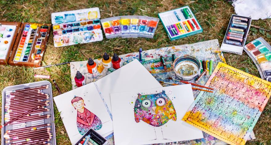 Farbkästen, Buntstifte, Wachsmalstifte und bunte Bilder auf einem Rasen