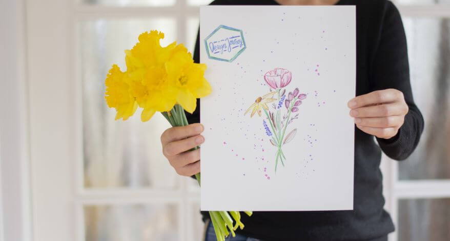 Eine Frau hält ein Blatt Papier mit gemaltem Blumenstrauß und einen echten Strauß Osterglocken in die Kamera.