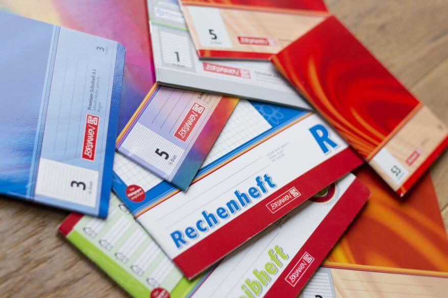 Mehrere Schulhefte mit unterschiedlichen Lineaturen von Brunnen liegen lose gestapelt auf einem Schreibtisch.