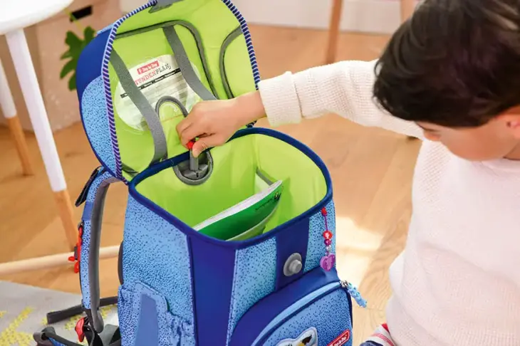 Ein Junge sitzt vor seinem geöffneten Step-by-Step Schulranzen und justiert mit einer Hand das Tragesystem nach.