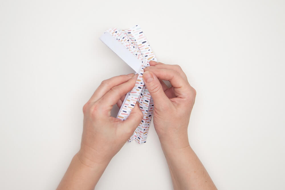 Pappvase: Hände falten ein Designpapier von Artoz nach Faltvorlage in eine Plisse-Form.