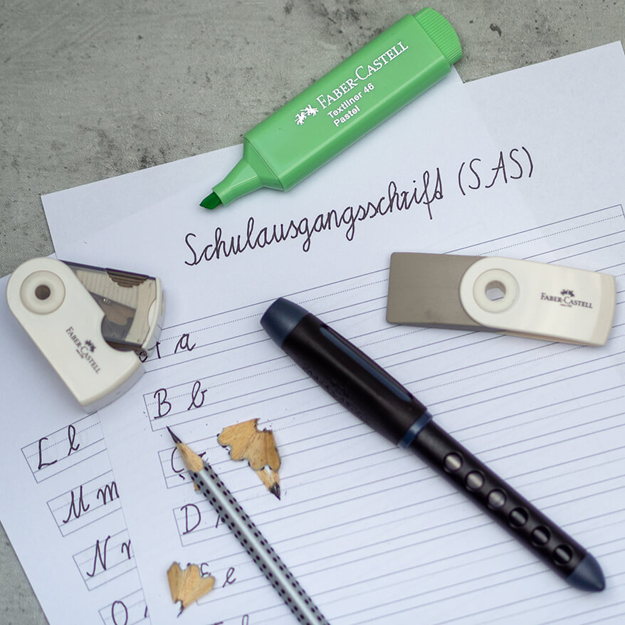 Auf einem Untergrund in Betonoptik liegen Übungsblätter für die Schulausgangsschrift. Darauf verteilt sind ein Spitzer, ein Radiergummi, ein Grip Bleistift, der Scribolino Schulfüller und ein grüner Textmarker von Faber-Castell. Foto: Johanna RundelAuf einem Untergrund in Betonoptik liegen Übungsblätter für die Schulausgangsschrift. Darauf verteilt sind ein Spitzer, ein Radiergummi, ein Grip Bleistift, der Scribolino Schulfüller und ein grüner Textmarker von Faber-Castell. Foto: Johanna Rundel