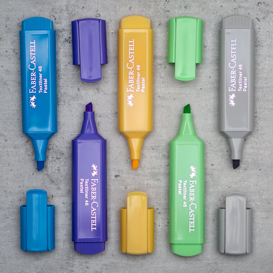 Ein blauer, violetter, gelber, grüner und grauer Textmarker von Faber-Castell liegen geöffnet und parallel mit ihren Deckeln angeordnet auf einem Untergrund in Betonoptik. Foto: Johanna Rundel