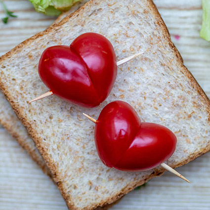 Zwei Scheiben Toastbrot liegen auf einem Holzbrett. Auf dem Brot sind zwei Tomatenherzen zu sehen, die mit einem Zahnstocher zusammengehalten werden. Foto: Johanna Rundel