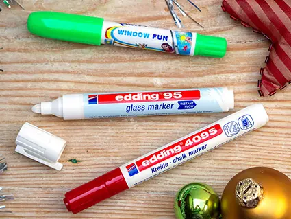 Drei edding Marker liegen auf einer Holzoberfläche. Etwas weihnachtliche Deko ist darum verteilt. Foto: Johanna Rundel