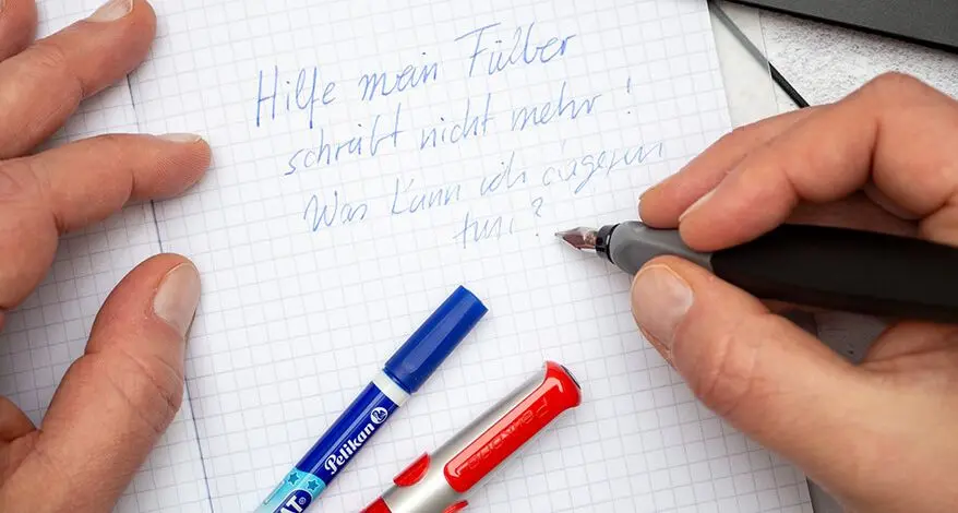 Jemand schreibt mit einem roten Füller von Pelikan in ein kariertes Notizbuch von herlitz. Foto: Johanna Rundel