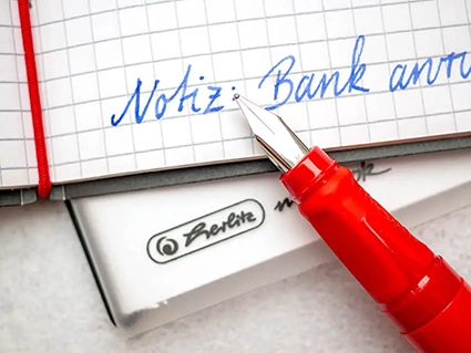 Ein roter Füller von Pelikan liegt auf einem aufgeschlagenen Notizheft von herlitz auf dem eine Notiz geschrieben steht. Foto: Johanna Rundel