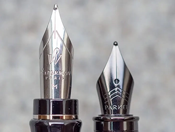 Eine Nahaufnahme von zwei Füllfederhalter-Spitzen. Man sieht die eingeprägten Logos von von Waterman und Parker, sowie das runde Korn an der Spitze. Foto: Johanna Rundel