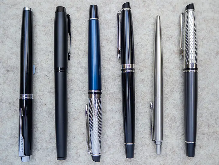 Sechs verschiedene Füllfederhalter und Kugelschreiber der Marken Waterman und Parker liegen symmetrisch nebeneinander aufgereiht auf einer hellen Filzmatte. Foto: Johanna Rundel